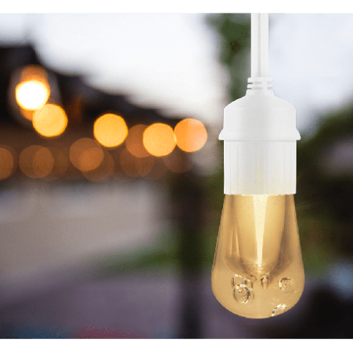 A bright light bulb with a warm glow hangs from a crisp white chord in front of other blurred outdoor lights