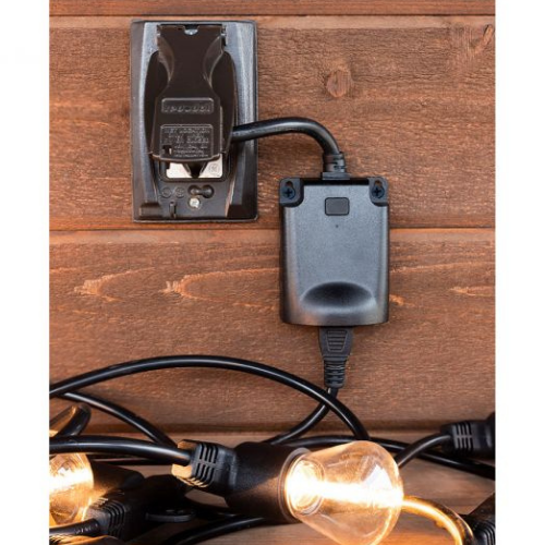 The black plug is connected to an on-wall outlet and is powering some warm-hued light bulbs